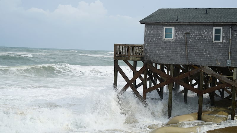Waves from Hurricane Erin crash against the sandbagged pilings of a building in Buxton, N.C.,...